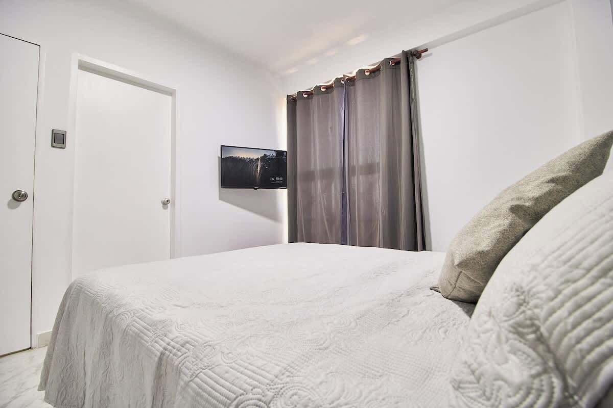 Une chambre d’hôtel avec un lit, un téléviseur fixé au mur, une porte et un rideau.