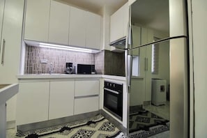 A compact kitchen with white cabinets, a microwave, a stove, and a refrigerator. - Margarita vista al mar Piscina y La Vela (Porlamar)