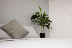 Ein Bett mit Kissen und einer Blumentopfpflanze daneben.