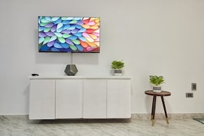 Ein modernes Interieur mit einem weißen Schrank, einem flachbildfernseher darüber montiert und einem kleinen runden Tisch mit einer Pflanze.