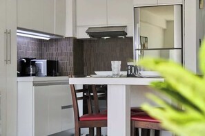 Eine moderne Küche mit weißen Schränken, einer Edelstahl-Dunstabzugshaube und einem Essbereich mit weißem Tisch und roten Stühlen.