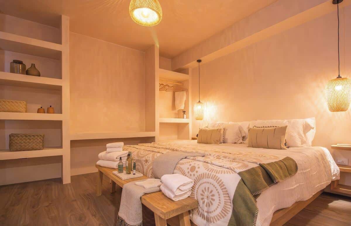 Ein Schlafzimmer mit einem großen Bett, Nachttischen, Ablageflächen mit Pflegeprodukten und einer Hängeleuchte.