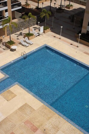 Ein Schwimmbecken mit Fliesen umgeben, mit Liegestühlen und Pflanzenkübeln.