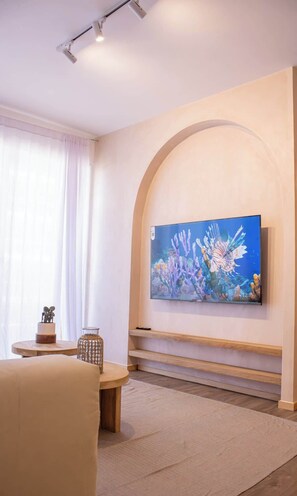 Un soggiorno moderno con una grande TV a schermo piatto montata a parete, un tavolo rotondo in legno, una poltrona imbottita e un vaso decorativo in vetro.