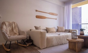 Ein Zimmer mit einer Couch, einem Schaukelstuhl, einem Holztisch und zwei Holzlöffeln an der Wand.