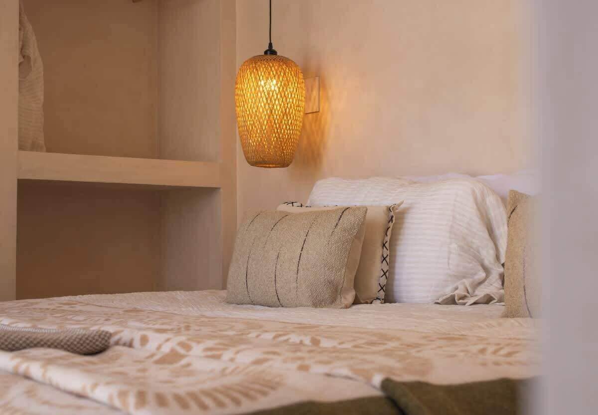 A bed with a patterned bedspread, two pillows, and a textured wall-mounted light fixture.