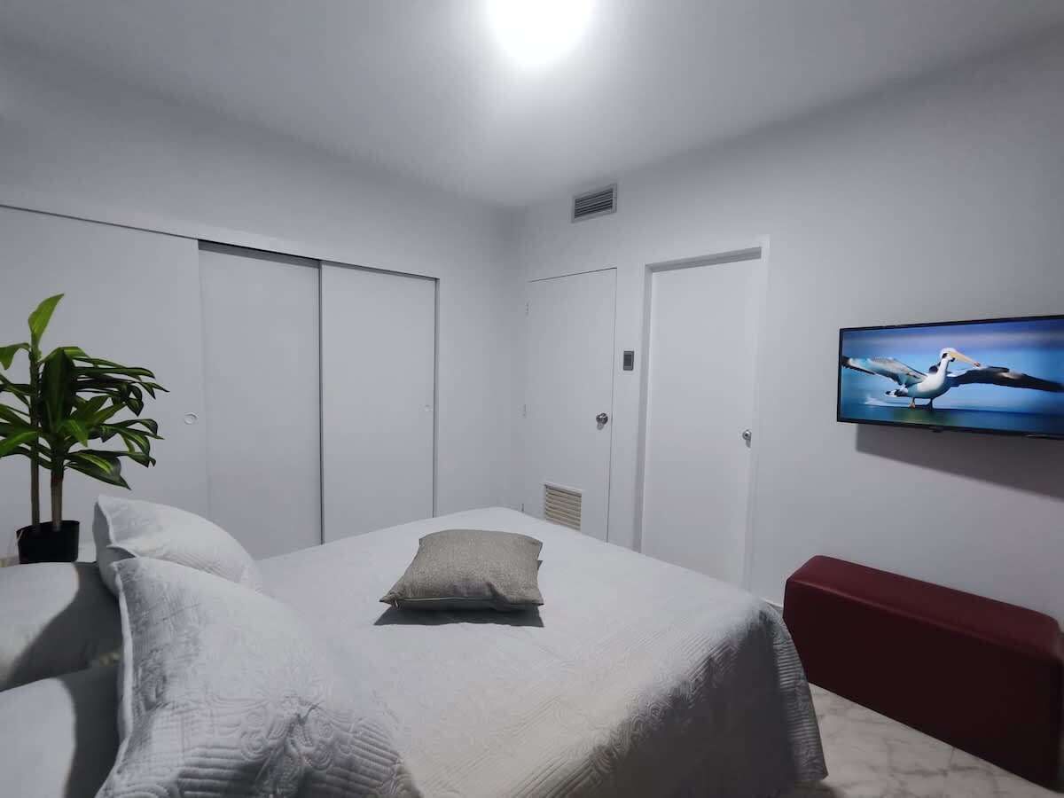 Een slaapkamer met een bed, een televisie, een plant en een rode bank.