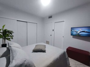 Une chambre à coucher avec un lit, une télévision, une plante et un banc rouge.