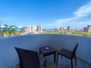 A balcony with two chairs and a small table, overlooking a cityscape with buildings and a construction crane. - Tus vacaciones perfectas a 360° (Porlamar Mariño)