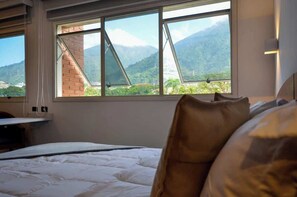 A bedroom with a bed, pillows, a desk, and a window with a mountain view. - Encanto Clásico en Altamira: Piso 4 con Balcón (Caracas)