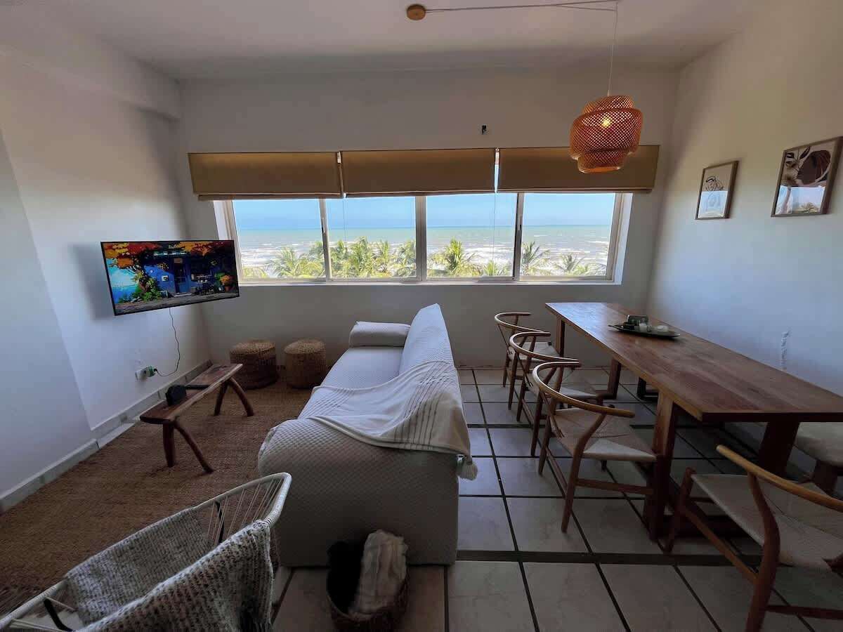 Une pièce comprenant un canapé, une table à manger, des chaises, un téléviseur et donnant sur l’océan.