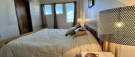 A hotel room with a bed, a bedside lamp, a window, and an air conditioning unit.