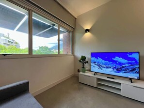 A modern living room with a flat-screen TV on a white entertainment unit, a potted plant, and a view of a building through a large window. - Elegante, moderno y práctico en Caracas (Caracas)