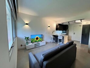 A modern living room with a flat-screen TV, a grey sofa, and a dining area with a white chair. - Elegante, moderno y práctico en Caracas (Caracas)