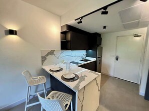 A modern kitchen with a marble countertop, two bar stools, a sink, and a door in the background.