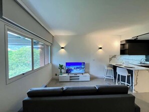 A modern living space with a flat-screen TV, a sofa, a dining area with bar stools, and a kitchen counter.