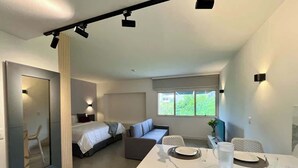 Et moderne interiør med seng, sofa, spisebord og et stort vindue.