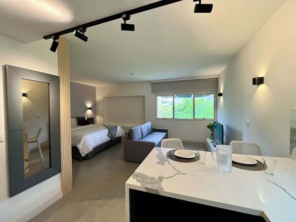 A modern interior with a bed, sofa, dining table, and a large window.