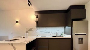 Et moderne køkken med en marmor bordplade, indbyggede skabe, en rustfri køleskab og en vægmonteret lampe.