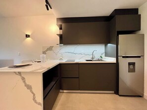 Eine moderne Küche mit Marmorarbeitsplatte, eingebauten Schränken, einem Edelstahlkühlschrank und einer Wandleuchte.