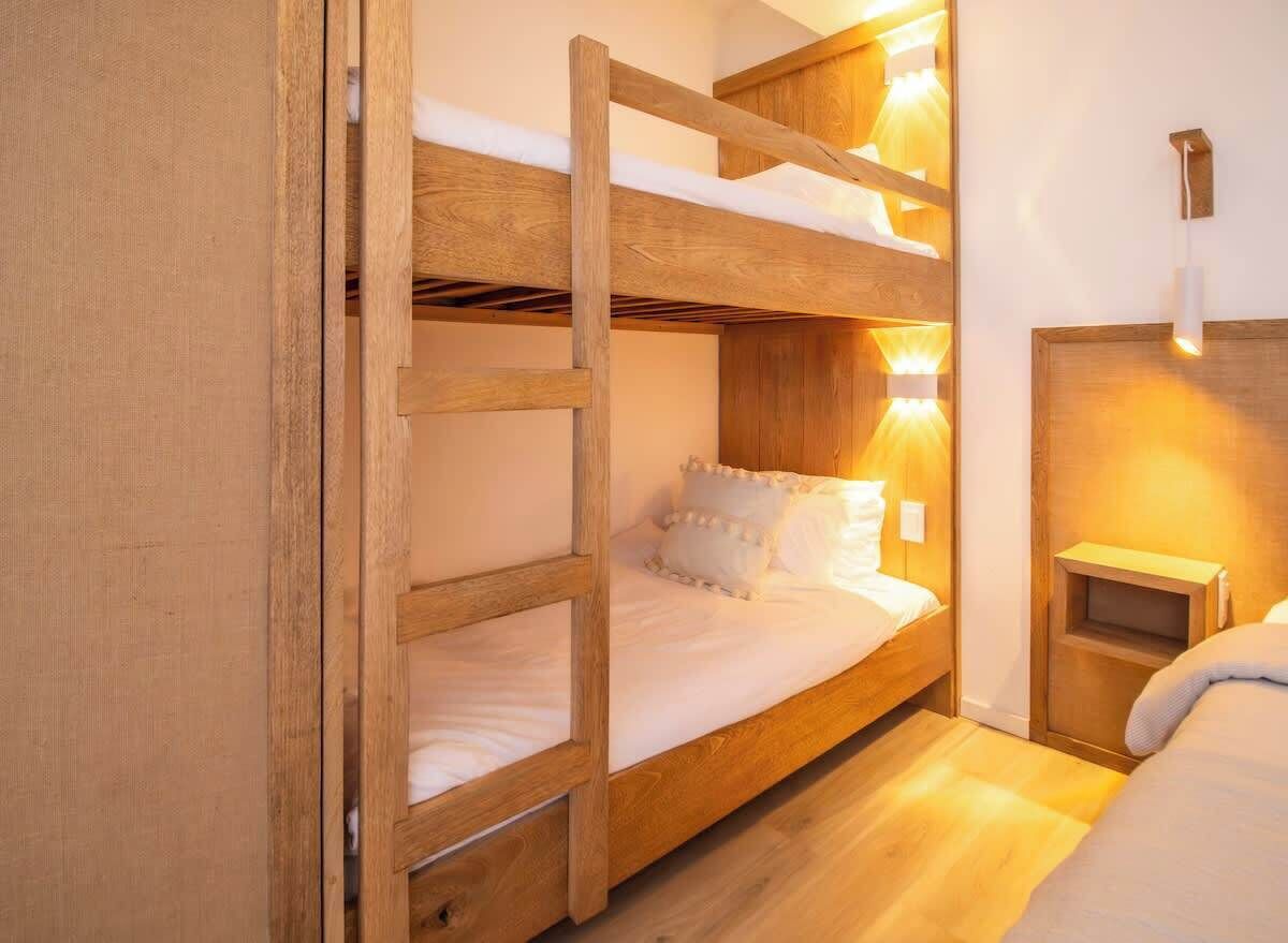 Une chambre avec un lit superposé, une tête de lit en bois, une table de chevet et un luminaire fixé au mur.