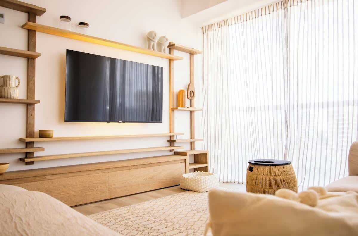 A modern living room with a large flat-screen TV mounted on a wooden wall unit, a comfortable sofa, and a small round table.