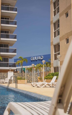 Un hôtel doté d’une piscine, de chaises longues et d’un panneau indiquant « GUUAQ ».