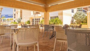 An outdoor seating area with chairs and tables, a tiled floor, and a building in the background.