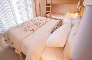 Ein ordentlich bezogenes Bett mit einem gemusterten Überwurf und Kissen, eine Holzleiter und eine Nachttischlampe.