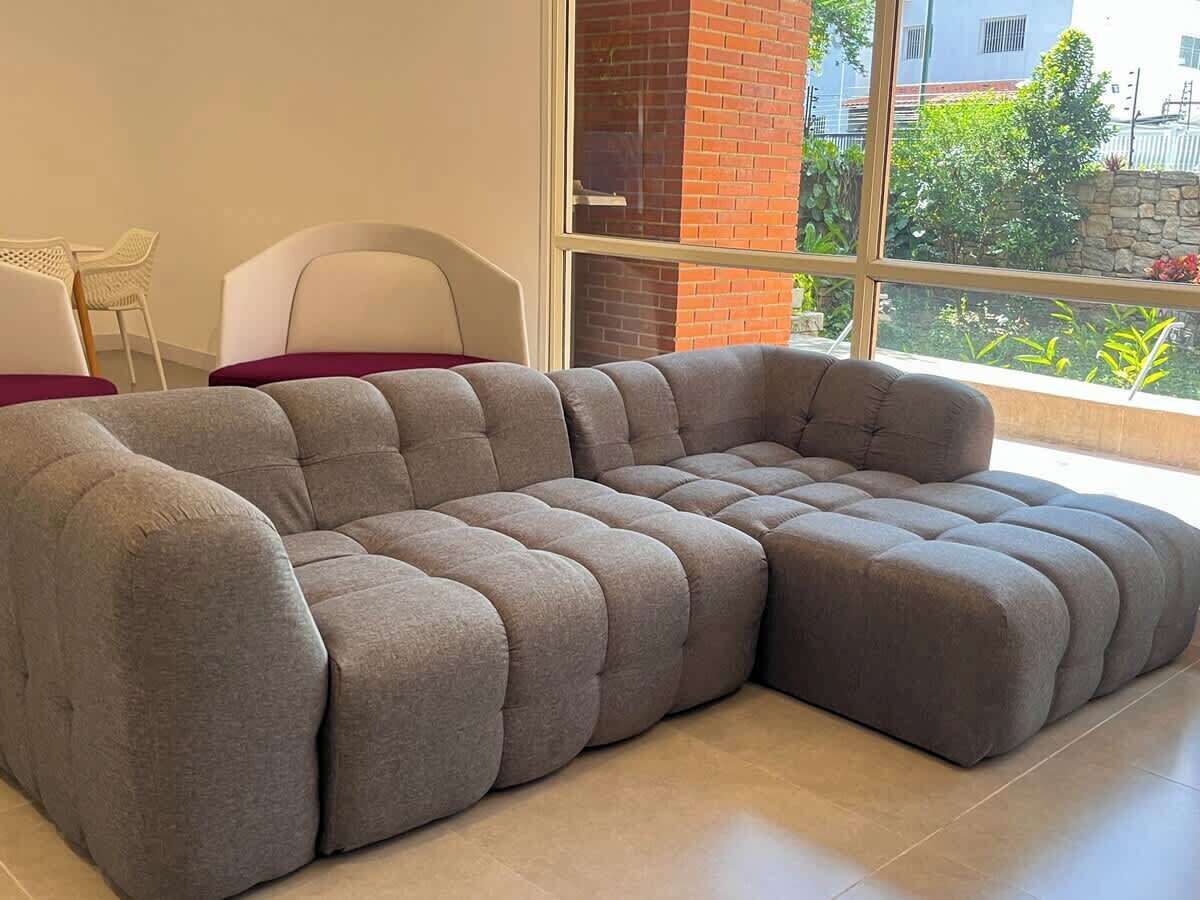 Ein modulares Sofa in einem Raum mit einem großen Fenster, einem weißen Sessel und einer Ziegelwand.