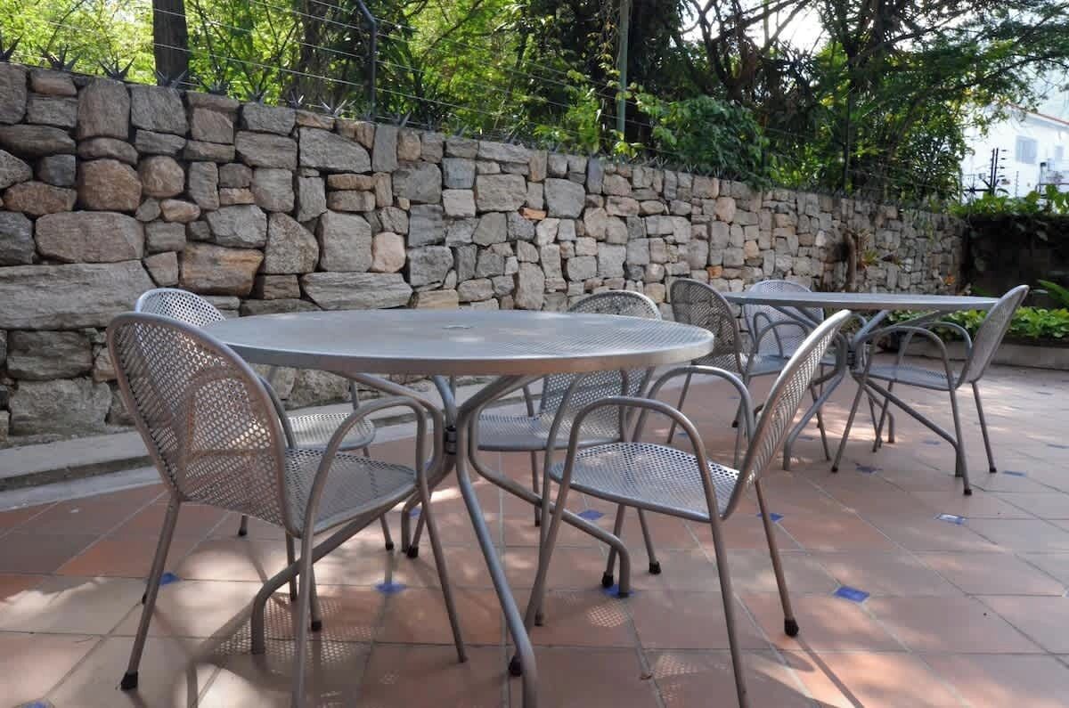 Een stenen muur, zitgedeelte buiten met metalen stoelen en tafels, en een betegeld terras.