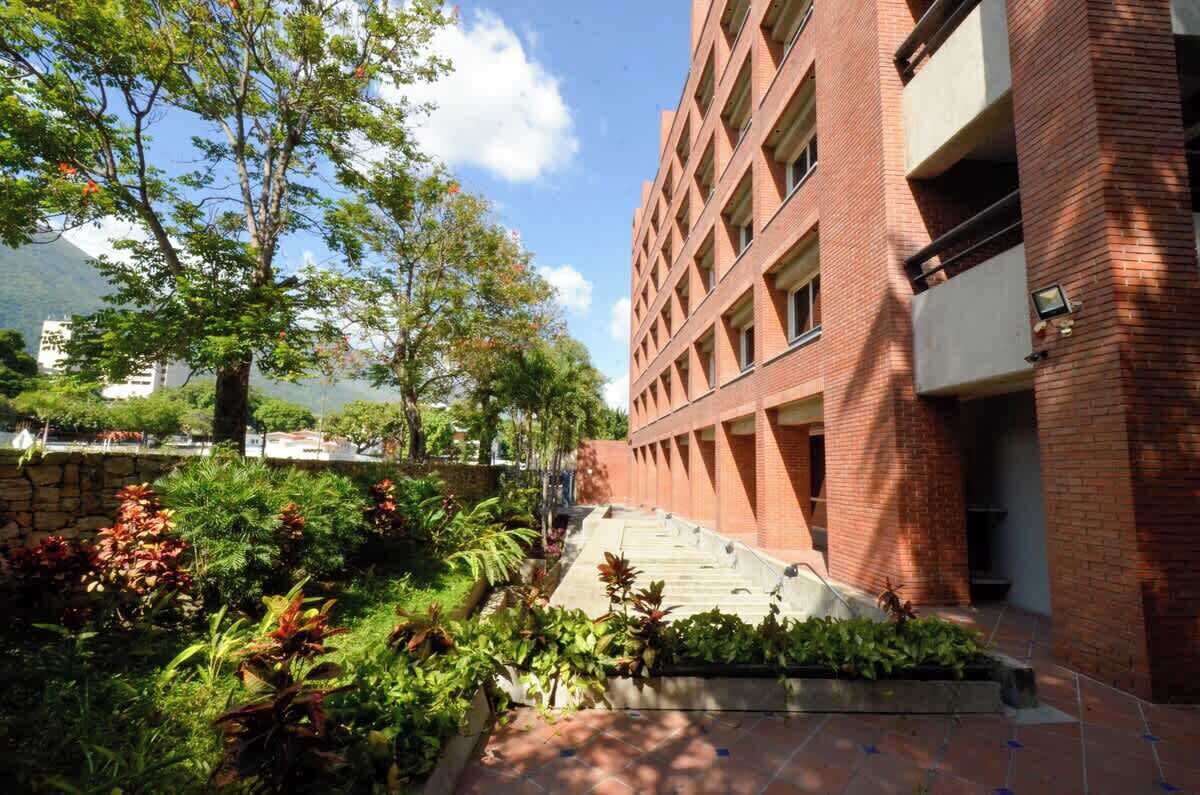 Un edificio con fachada de ladrillo, una escalera que sube a un nivel superior y un jardín con diversas plantas.
