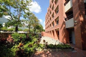 A building with a brick facade, a staircase leading to an upper level, and a garden area with various plants.