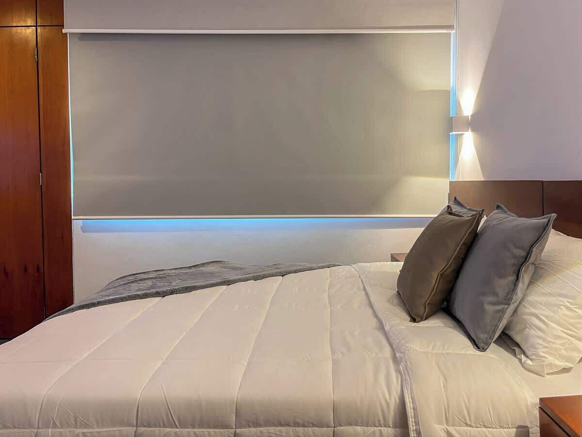 A hotel room with a large bed, a headboard with integrated lighting, and a wooden wardrobe.