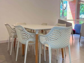 A dining area with a round table and white chairs with wooden legs. - Tu Rincón Altamira - Nomad Suites (Caracas)