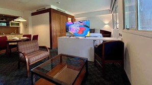 Quarto de hotel com televisão, área de jantar, sofá e uma pequena mesa.