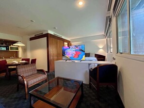 Ein Hotelzimmer mit Fernseher, Essbereich, einer Couch und einem kleinen Tisch.