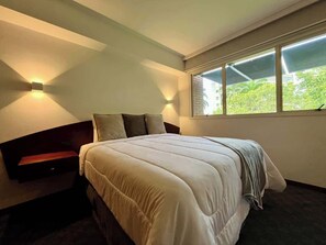 A modern bedroom with a large bed, bedside lamps, a bench, and a window with a view. - Altamira Apt w/ Balcony & High-Speed WiFi (Caracas)