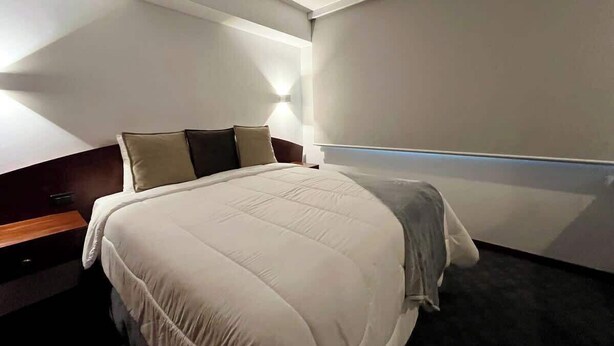 Quarto de hotel com cama, mesas de cabeceira e luminária na parede.