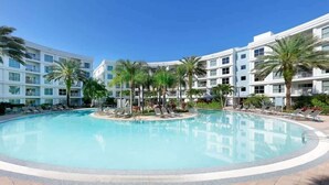 A hotel with a central swimming pool surrounded by palm trees and lounge chairs. - 2BR Pool View Suite Near Walt Disney World Resort (Kissimmee)
