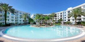 Ein Hotel mit einem zentral gelegenen Schwimmbad, umgeben von Palmen und Liegestühlen.