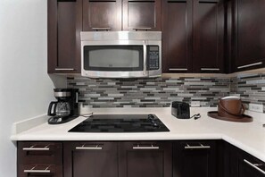 Eine moderne Küche mit dunklen Holzschränken, einer Edelstahl-Mikrowelle, einer schwarzen Induktionskochplatte, einer Kaffeemaschine und einem Toaster.
