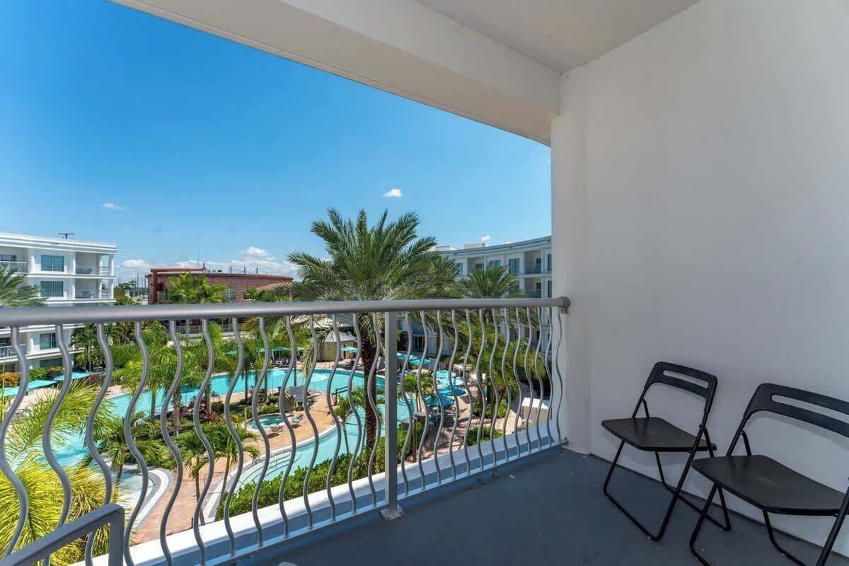 A balcony with a view of a swimming pool and palm trees, two chairs, and a railing.