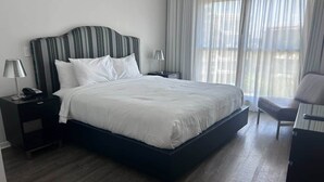 A hotel room with a large bed, two bedside tables, a chair, and a window with curtains. - 2BR Pool View Suite Near Walt Disney World Resort (Kissimmee)