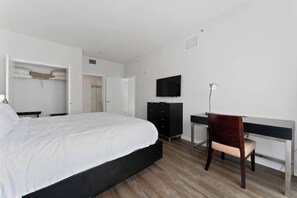Quarto de hotel com cama, escrivaninha, cadeira, televisão e guarda-roupa.