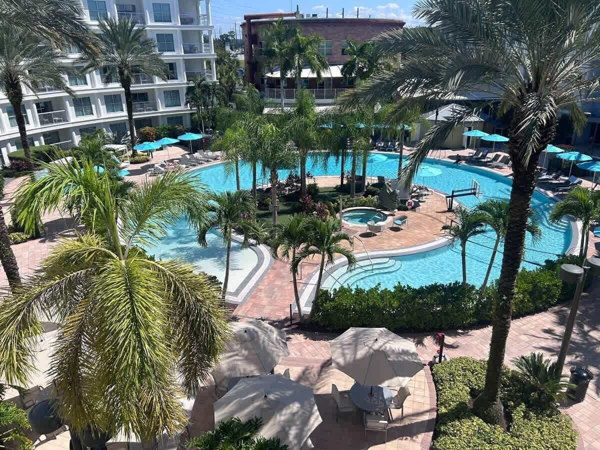 A resort pool area with multiple swimming pools, palm trees, and lounge chairs.