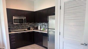 A modern kitchen with dark cabinetry, a stainless steel refrigerator, and a microwave. - 2BR Pool View Suite Near Walt Disney World Resort (Kissimmee)