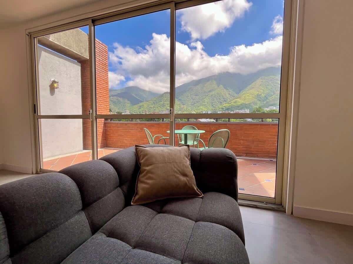 A room with a sofa and a view of a balcony with a table and chairs.