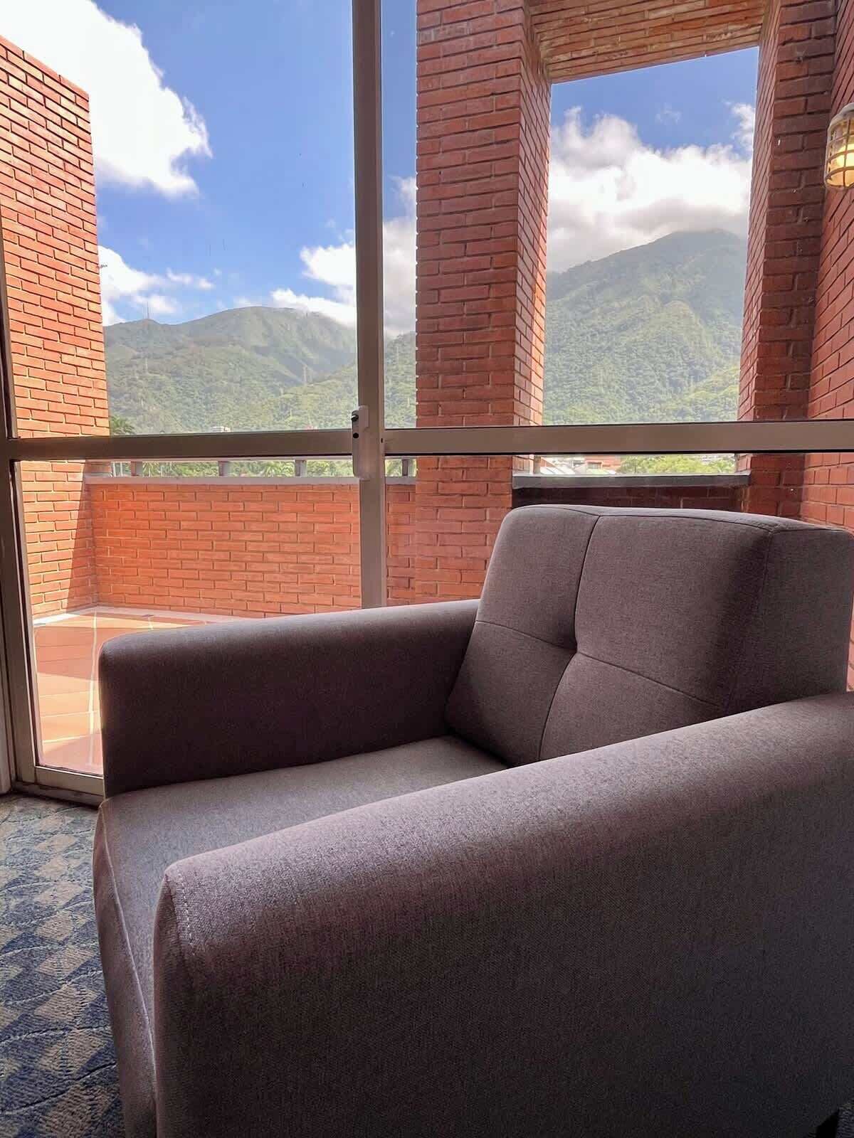 A room with a sofa facing a large window overlooking mountains.