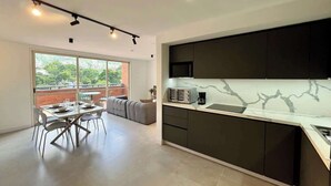 Una cucina moderna con mobili scuri e un piano di lavoro in marmo, una zona pranzo con tavolo e sedie, e un'ampia finestra vista su del verde.